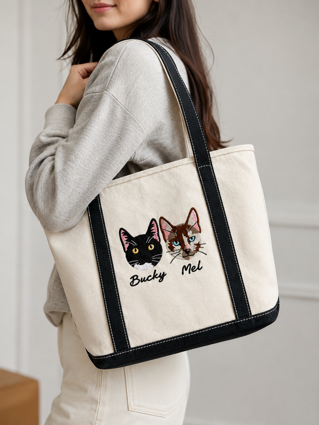 custom-pet-portrait-embroidered-tote-bag-model - MONSTERiSH Woman carrying a custom pet portrait embroidered canvas tote bag featuring two personalised cat portraits and names